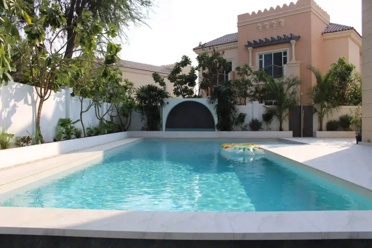 Modern custom concrete swimming pool with coping and surrounding garden landscape in a Dubai villa.