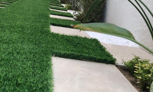 Close-up of artificial grass with large beige stone stepping path in modern narrow side garden with tall cypress trees - side yard landscaping Dubai