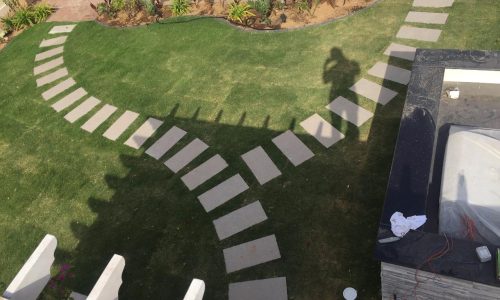 Aerial view of curved stepping stone pathway on lush green villa lawn with tropical plants and modern garden design - villa landscaping Dubai