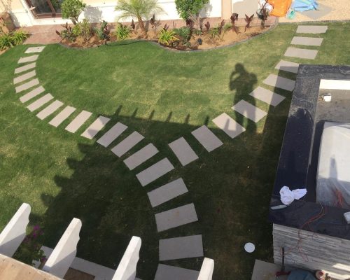 Aerial view of curved stepping stone pathway on lush green villa lawn with tropical plants and modern garden design - villa landscaping Dubai