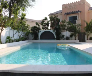 Modern custom concrete swimming pool with coping and surrounding garden landscape in a Dubai villa.
