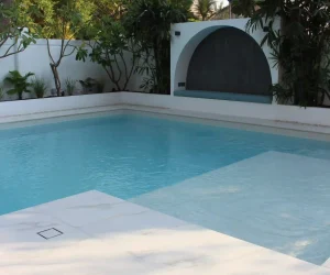 Clean poolside hardscape deck with boundary palm trees and clear blue pool water in a Dubai villa backyard.
