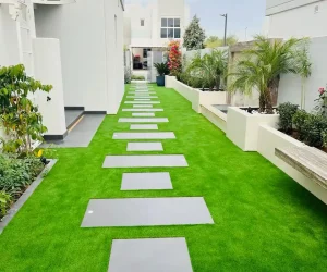 Geometric paving stone walkway integrated with green artificial grass and modern planters in a Dubai residential landscaping project.